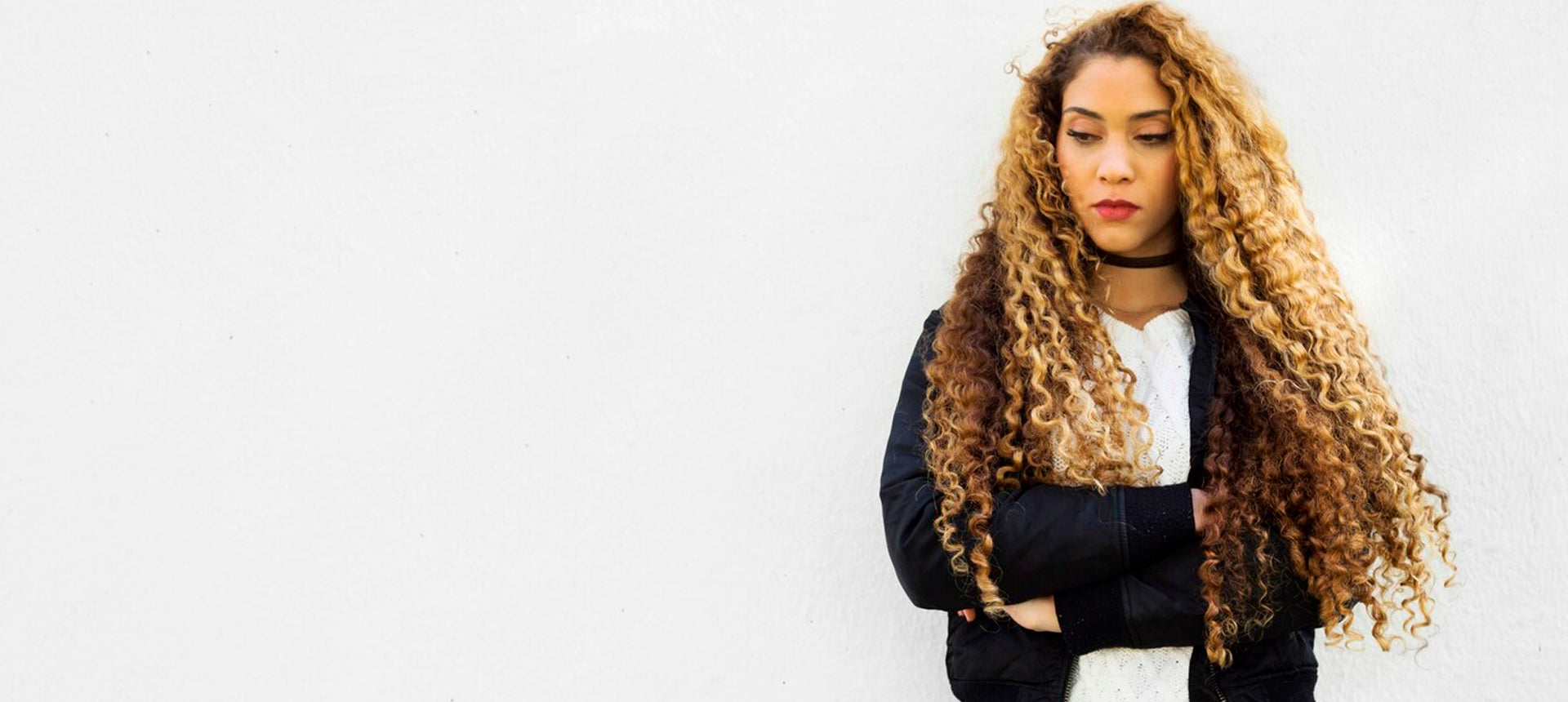 Woman with long, curly hair wearing a black jacket against a white background