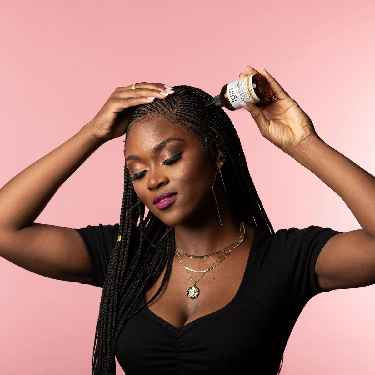 TGIN Jamaican Black Castor Oil Growth Serum 4 oz — model applying serum to scalp between braids