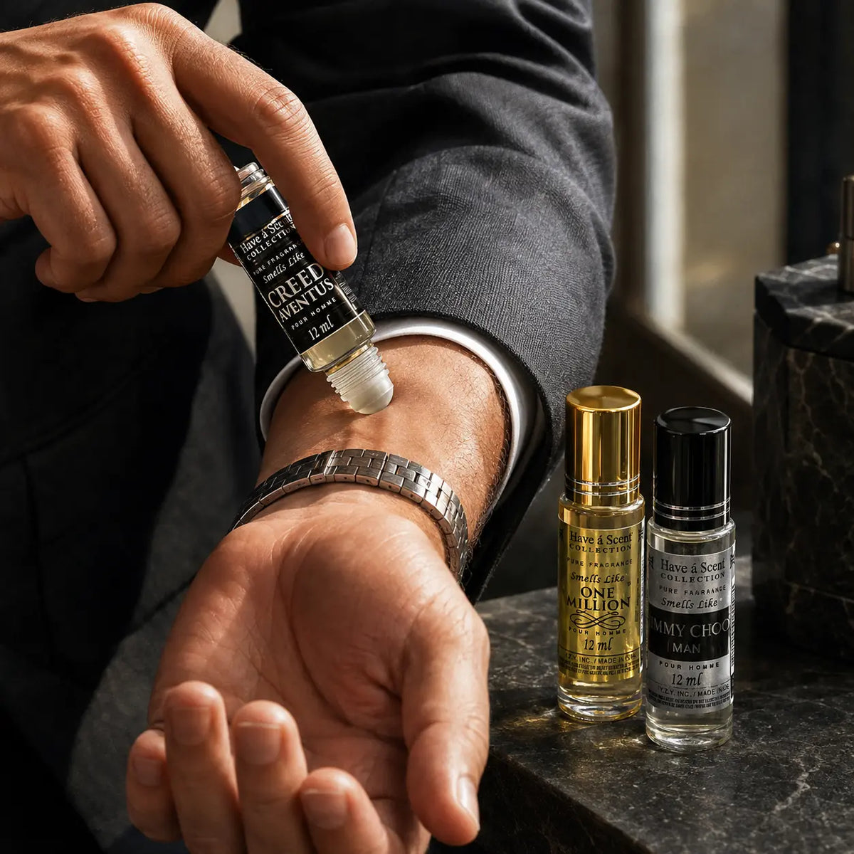 A close-up lifestyle shot of a man applying a roll-on perfume oil to his wrist. Two small glass perfume bottles, one with a gold cap and one with a black cap, are standing on a dark marble surface next to him.