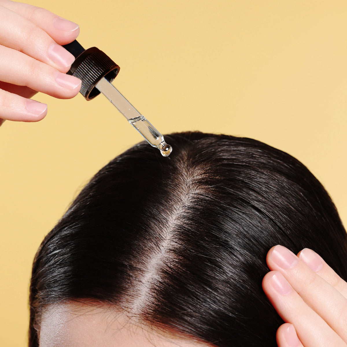 Dropper applying Tyche Turmeric Oil along a hair part