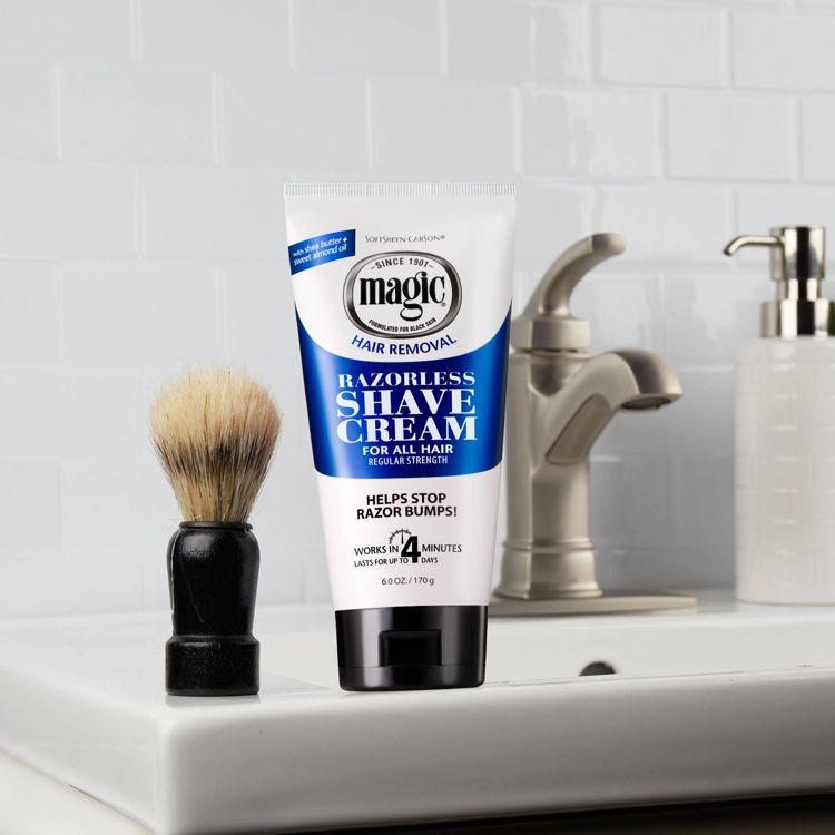 A tube of Magic Razorless Shave Cream for all hair, regular strength, 6 oz, is placed on a bathroom counter next to a shaving brush.