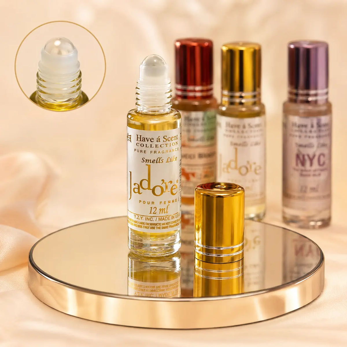 A set of 'Have & Scent' brand perfume rollerball bottles displayed on a round mirrored tray. The main bottle in the foreground is labeled 'Jadôre Pour Femme' with its gold cap removed and placed beside it.