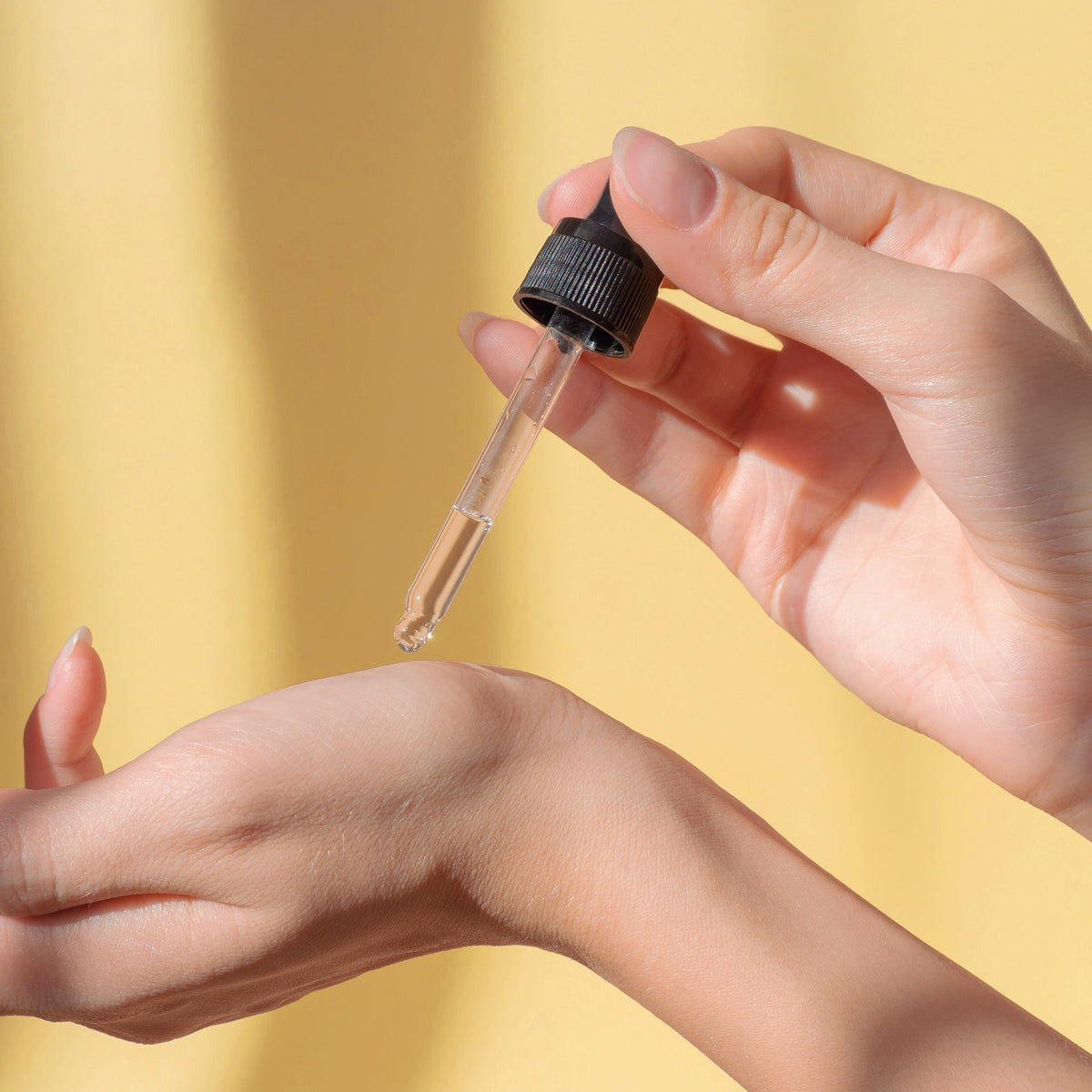 Dropper dispensing oil onto the back of a hand