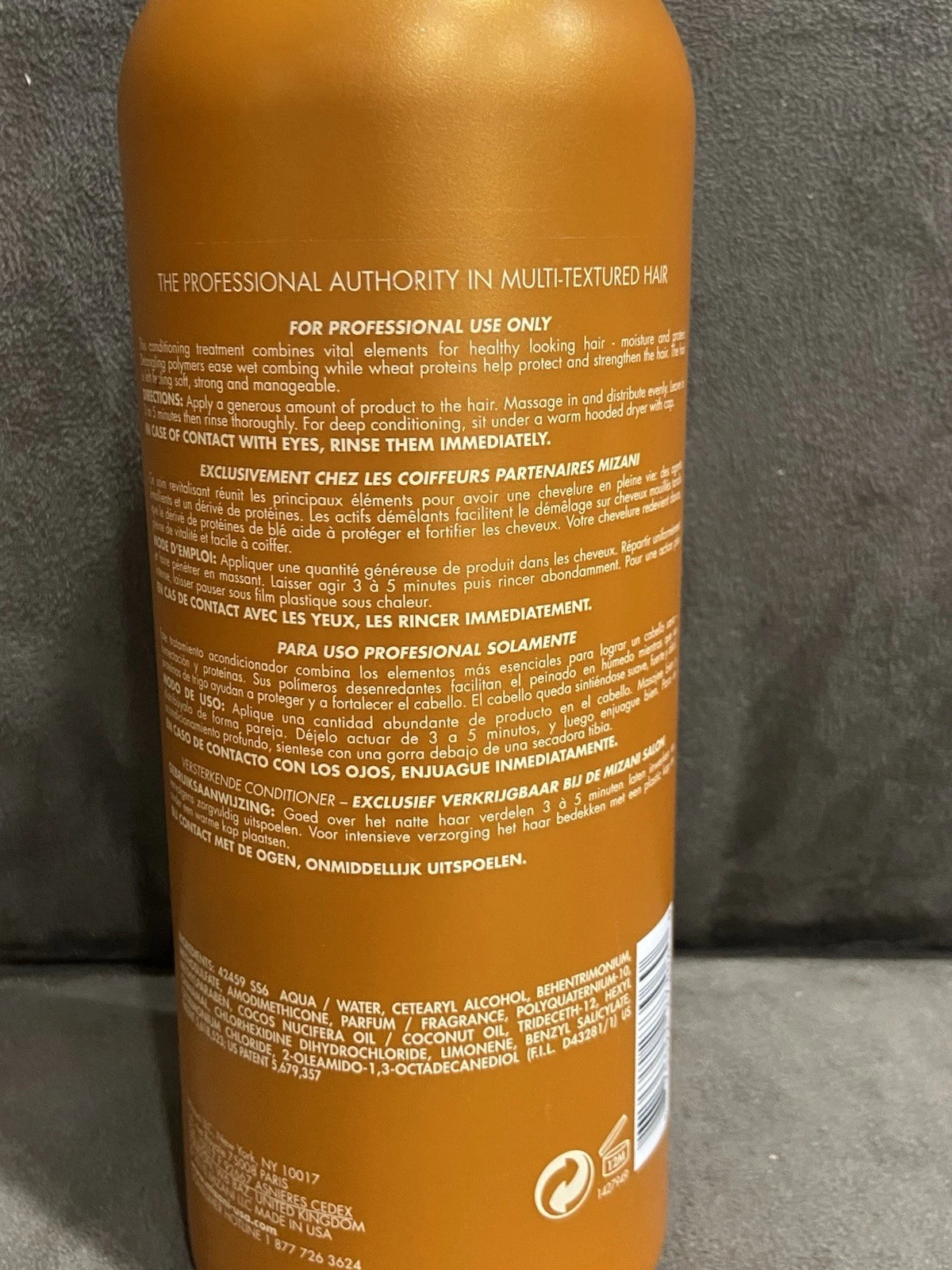 Orange MIZANI Thermasmooth Conditioner bottle with white text, 33.8 oz label, and black barcode on pink carpet background.