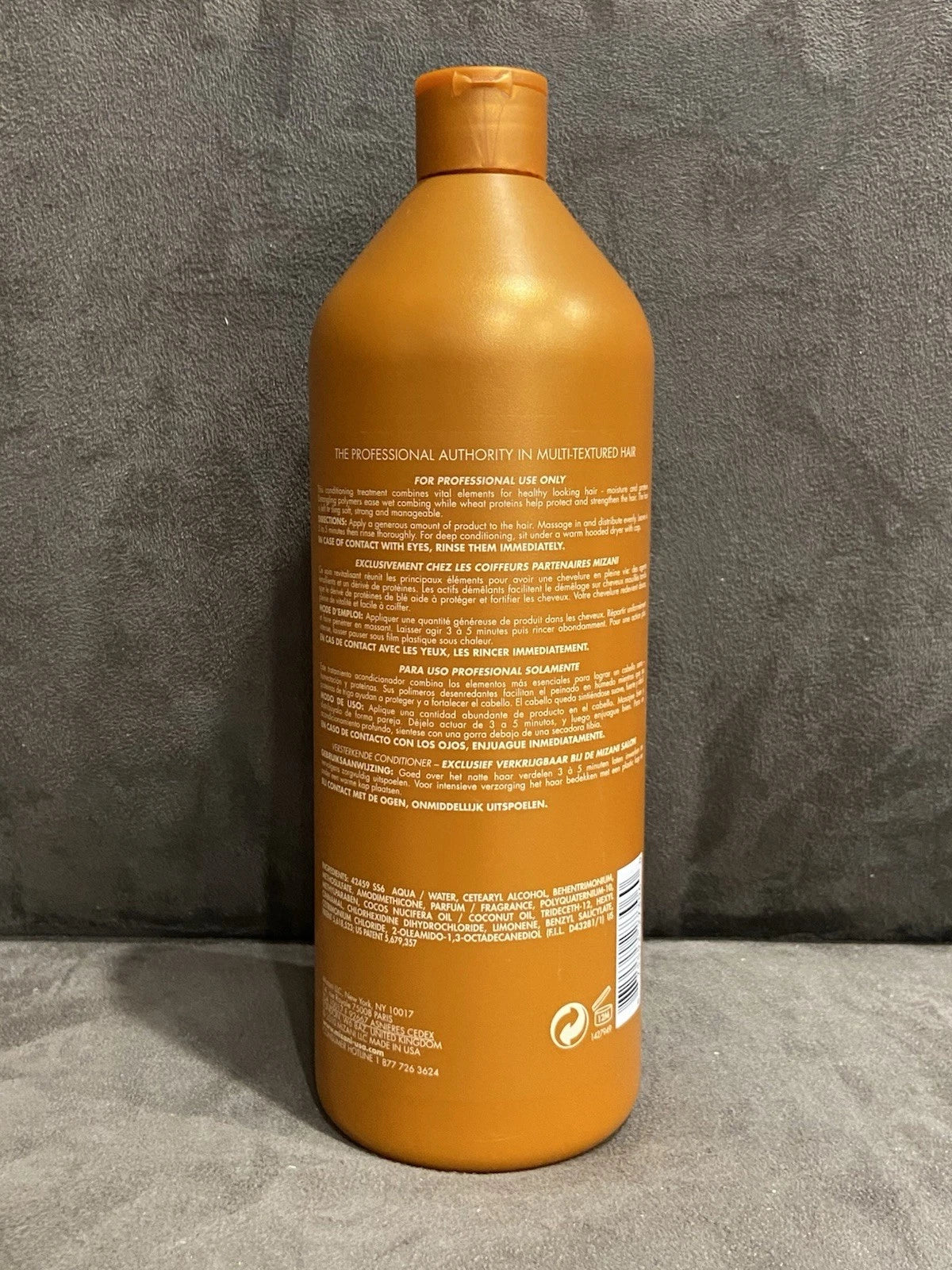 Orange MIZANI Thermasmooth conditioner bottle with white text, 33.8 oz label, and yellow cap on a gray surface.